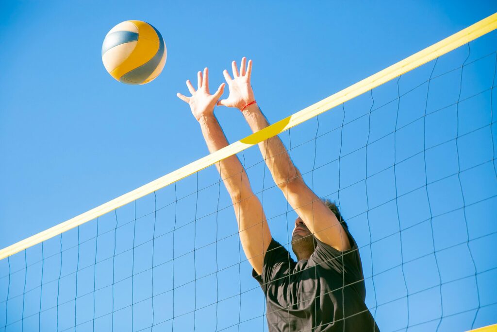 pexels-photo-6180408-6180408 Dynamic outdoor volleyball game with a male player blocking a ball under clear blue skies.