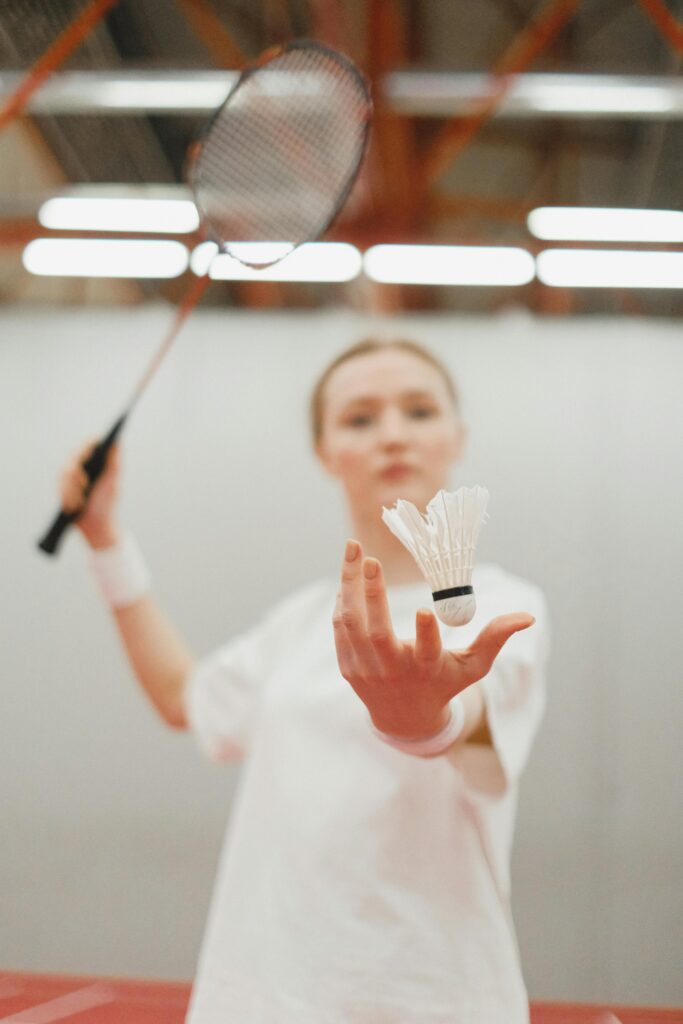 A young female badminton player holding a shuttlecock on an indoor court.